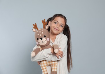 Photo of Cute girl in white pajamas with toy deer on light grey background