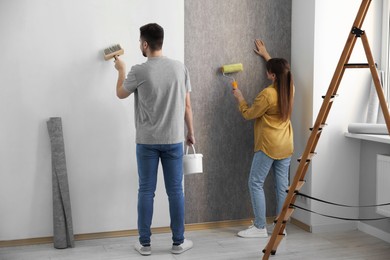 Woman and man hanging wallpaper in room, back view