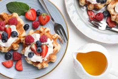 Photo of Delicious Belgian waffles with whipped cream and berries served on white table, flat lay