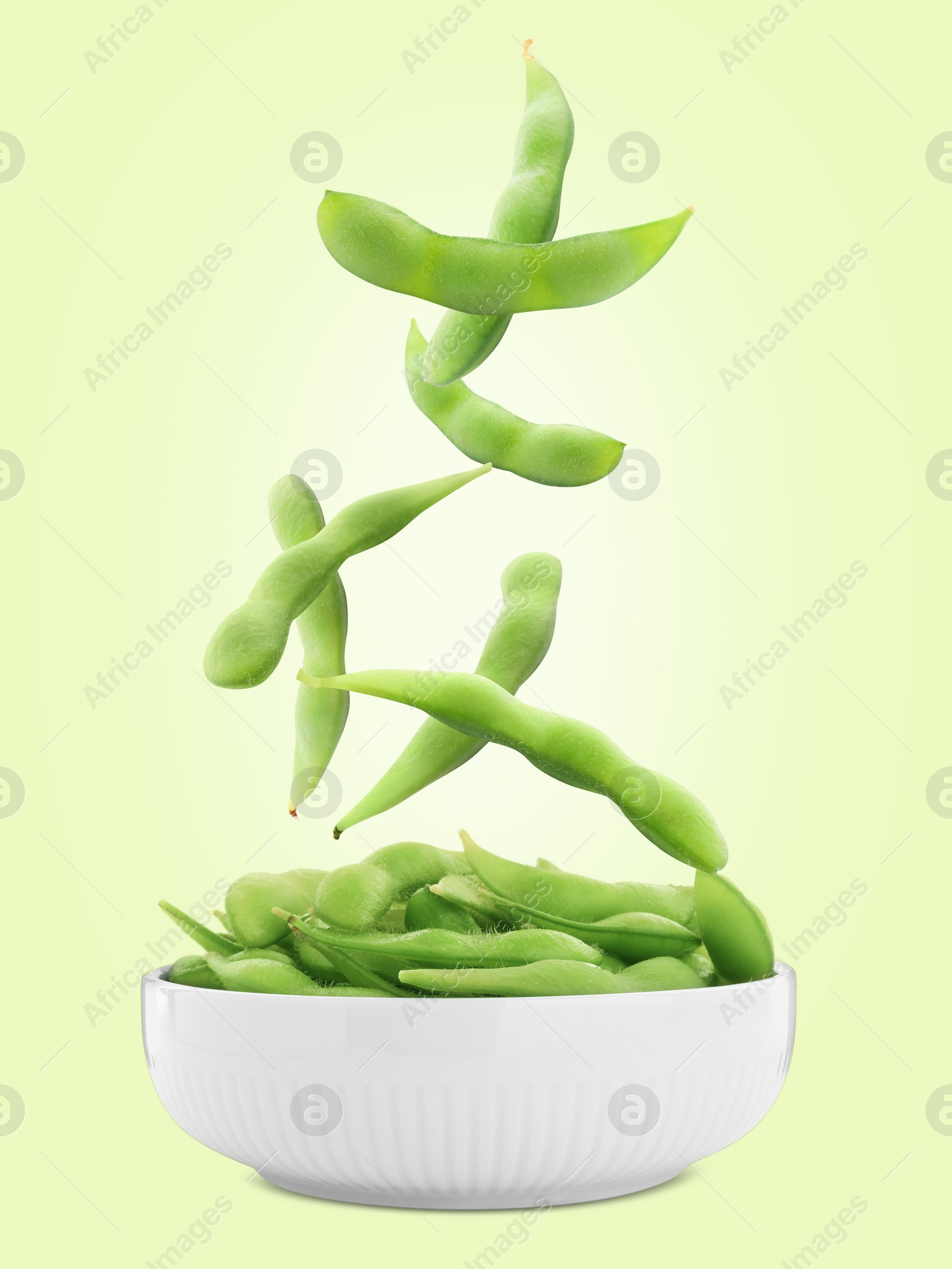 Image of Edamame pods falling into bowl on light green background