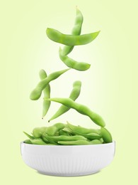 Image of Edamame pods falling into bowl on light green background