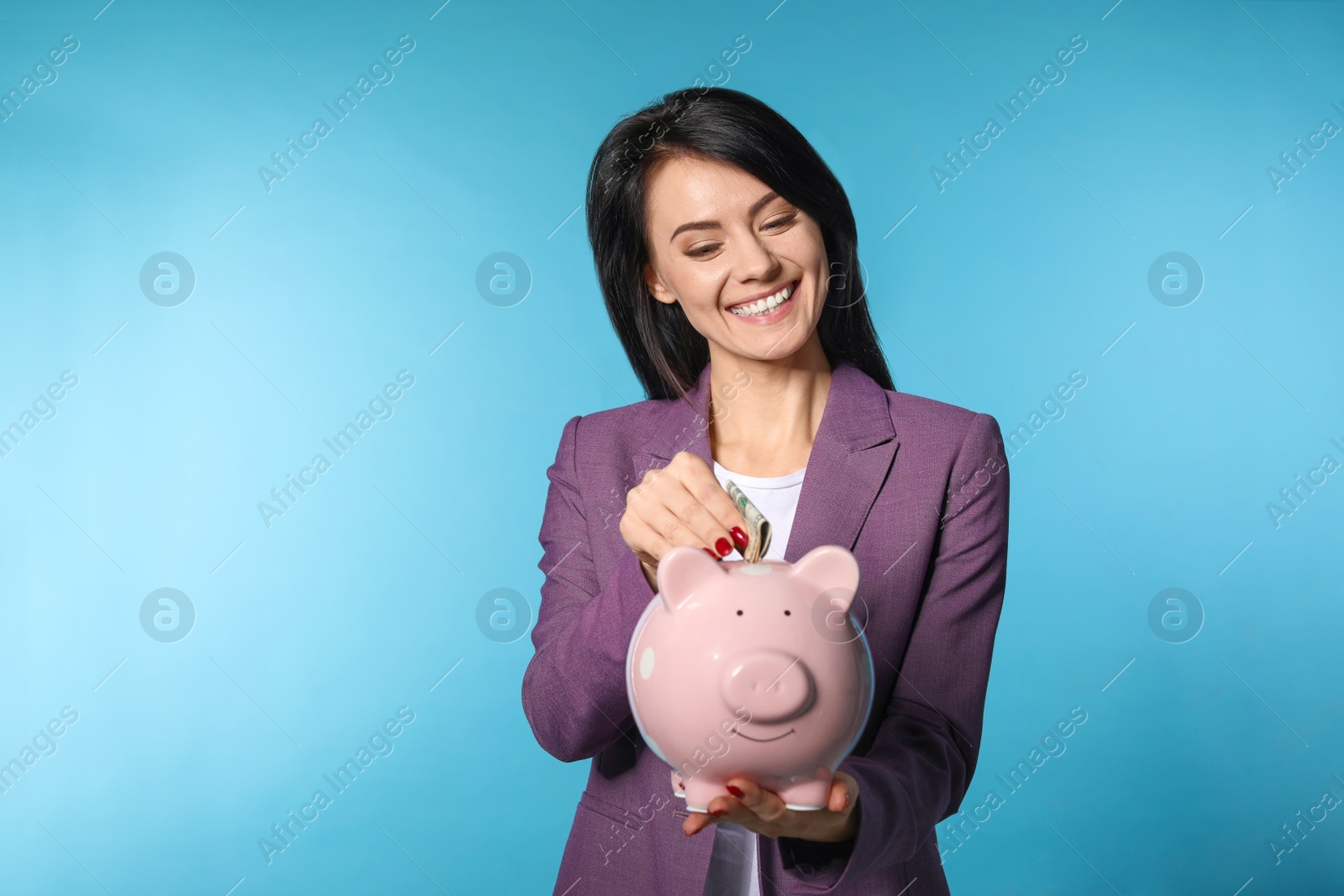 Photo of Beautiful businesswoman putting money into piggy bank on color background