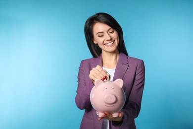 Photo of Beautiful businesswoman putting money into piggy bank on color background