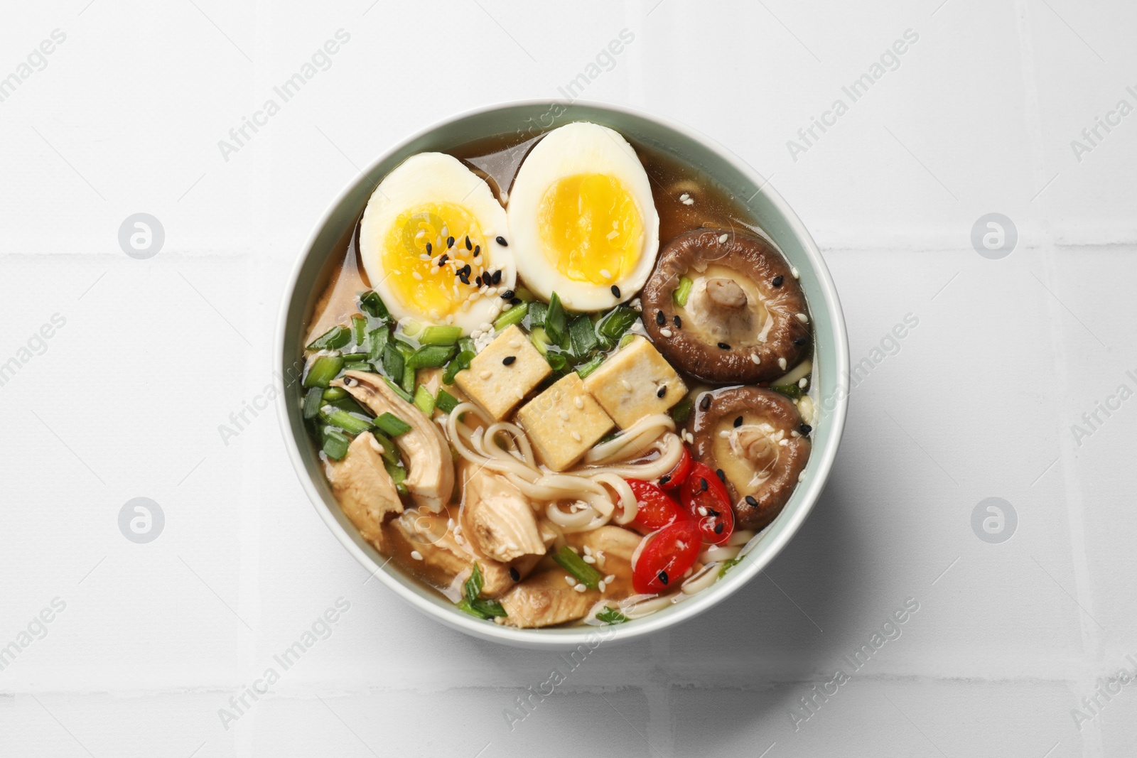 Photo of Noodle soup. Bowl of delicious ramen on white tiled table, top view