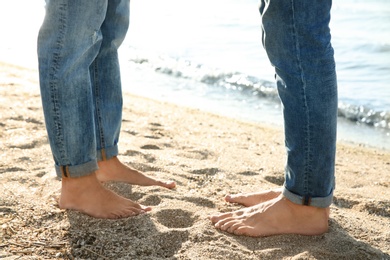 Gay couple standing barefoot on beach, closeup
