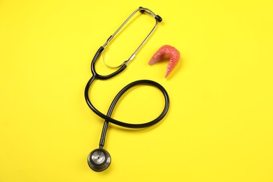 Photo of Endocrinology. Stethoscope and model of thyroid gland on yellow background, top view
