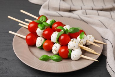 Caprese skewers with tomatoes, mozzarella balls, basil and spices on grey wooden table, closeup