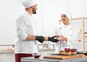 Photo of Pastry chefs preparing desserts at table in kitchen