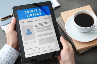 Photo of Man holding tablet with driver's license application form at grey table, closeup