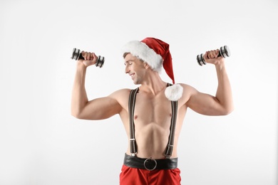 Photo of Young muscular man in Santa hat with dumbbells on white background
