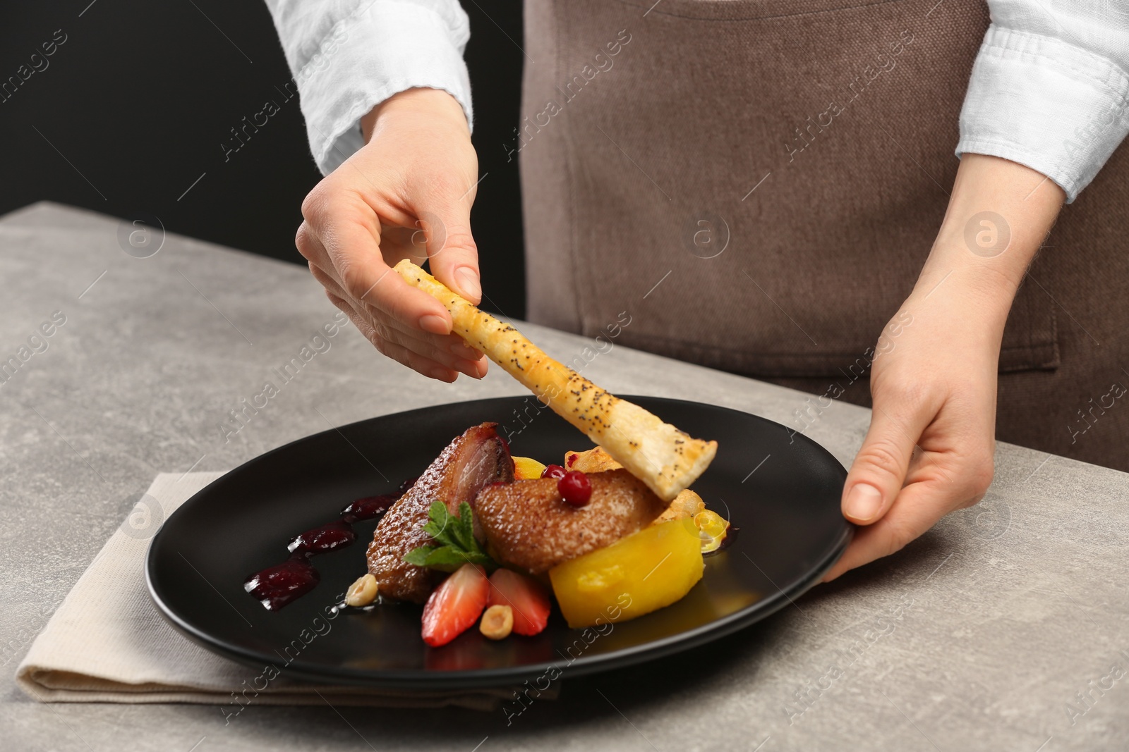 Photo of Food stylist preparing delicious dish with chicken, parsnip and strawberries for photoshoot at grey table in studio, closeup