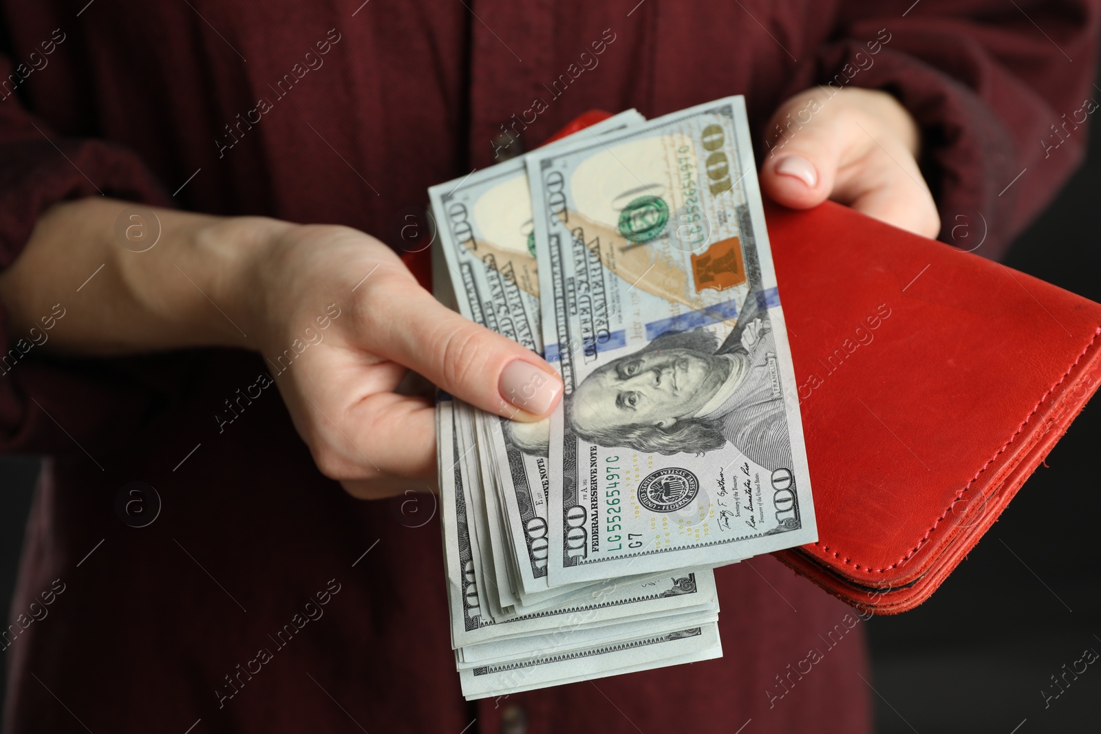 Photo of Money exchange. Woman putting dollar banknotes into wallet on dark background, closeup