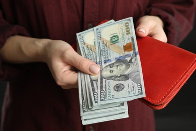 Money exchange. Woman putting dollar banknotes into wallet on dark background, closeup