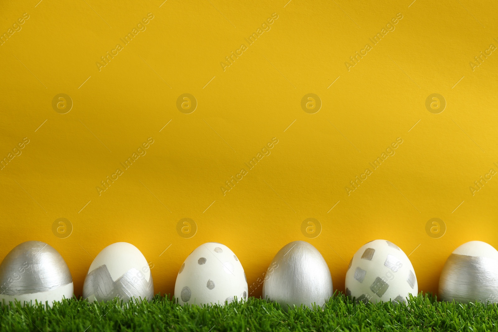 Photo of Line of painted Easter eggs on green lawn against color background, space for text