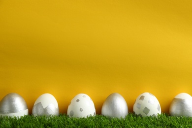 Line of painted Easter eggs on green lawn against color background, space for text