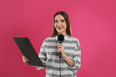 Photo of Young female journalist with microphone and clipboard on pink background