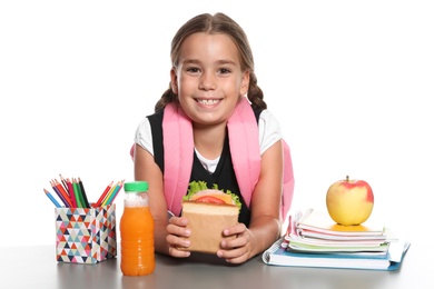 Photo of Schoolgirl with healthy food and backpack sitting at table on white background