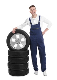 Male mechanic with car tires on white background