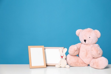 Photo frames and adorable toys on table against color background, space for text. Child room elements