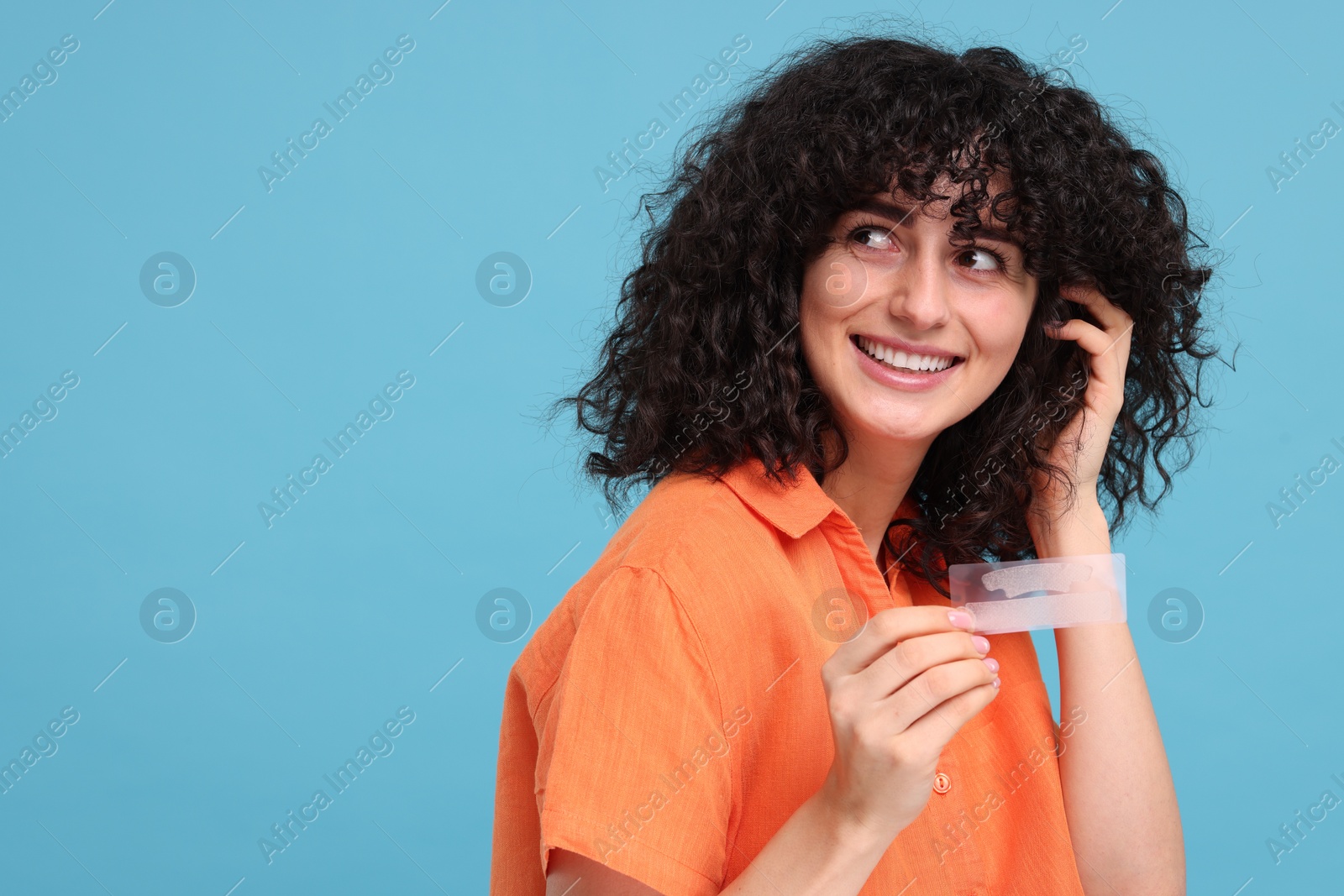 Photo of Young woman holding teeth whitening strips on light blue background, space for text