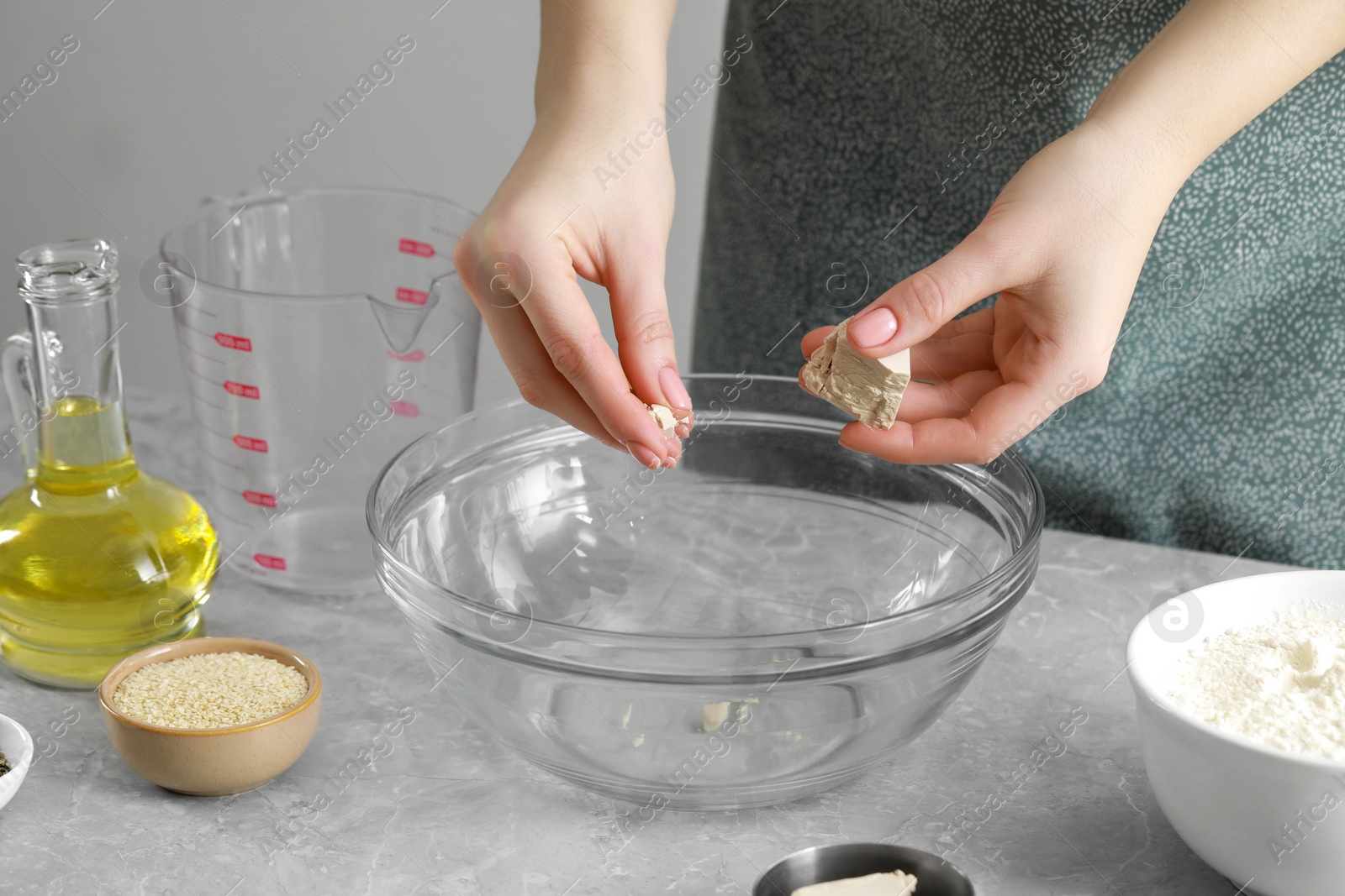 Photo of Woman adding yeast into bowl at light grey marble table indoors, closeup. Cooking traditional grissini