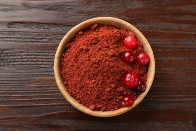 Photo of Dried cranberry powder and fresh berries in bowl on wooden table, top view