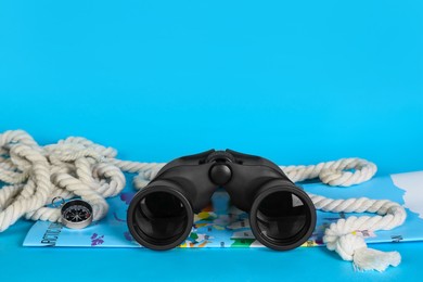 Photo of Modern binoculars, rope, map and compass on light blue background, space for text