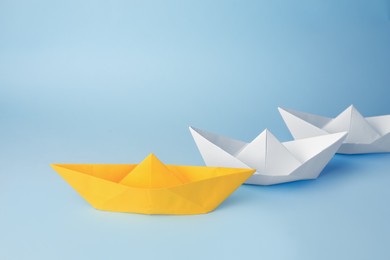 Group of paper boats following yellow one on light blue background. Leadership concept