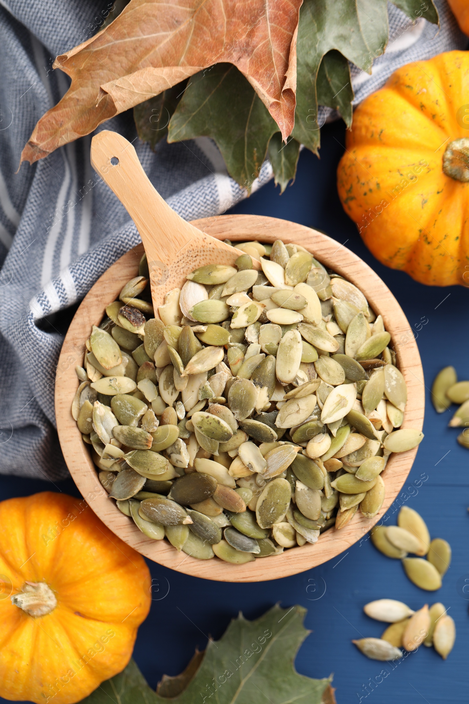 Photo of Bowl with seeds, fresh pumpkins and dry leaves on blue wooden table, flat lay