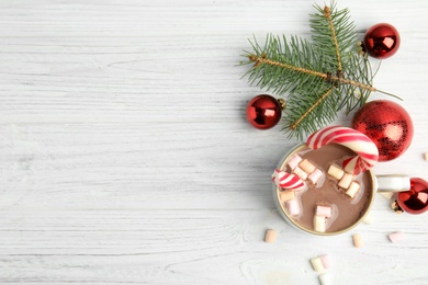 Photo of Cup of tasty cocoa with marshmallows, candy cane and Christmas decor on white wooden table, flat lay. Space for text
