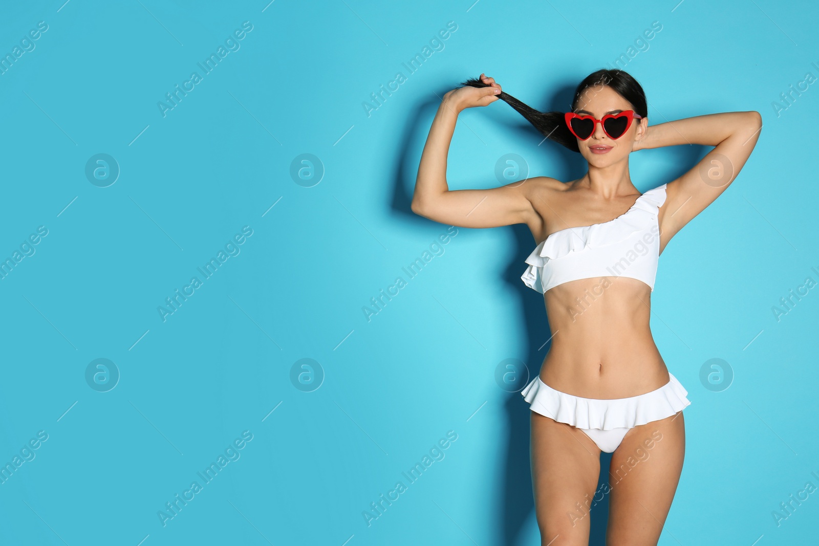 Photo of Beautiful young woman in white bikini with sunglasses on light blue background. Space for text