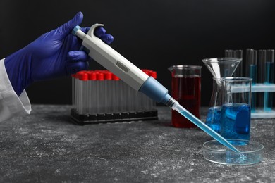 Laboratory analysis. Scientist dripping sample with micropipette into petri dish at grey table, closeup