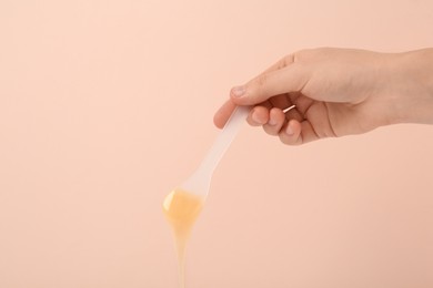 Woman holding spatula with hot depilatory wax on beige background, closeup. Space for text