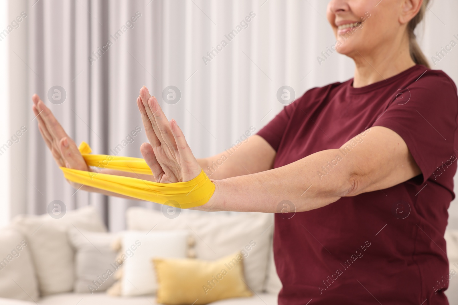 Photo of Senior woman doing exercise with fitness elastic band at home, closeup