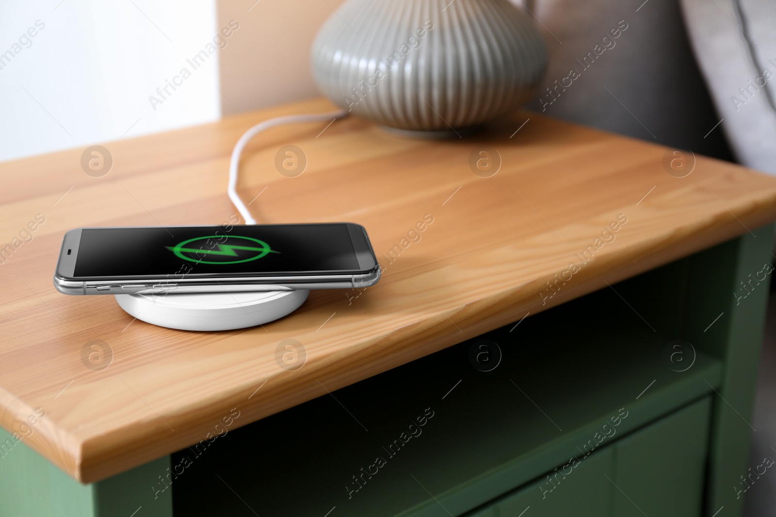 Photo of Smartphone charging on wireless pad in room. Space for text