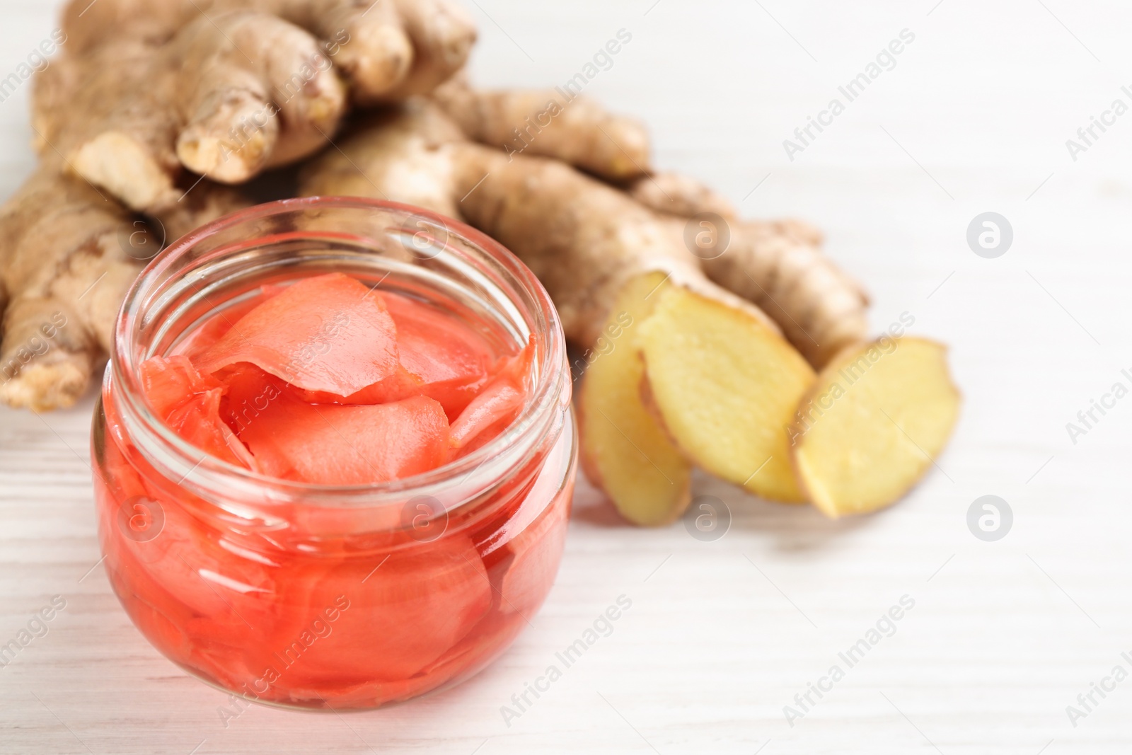 Photo of Spicy pickled ginger and root on white wooden table, space for text