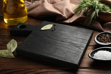 Photo of Black cutting board, salt, pepper and bay leaves on wooden table. Space for text