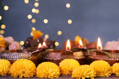 Photo of Diwali celebration. Diya lamps and chrysanthemum flowers on table against blurred lights, closeup