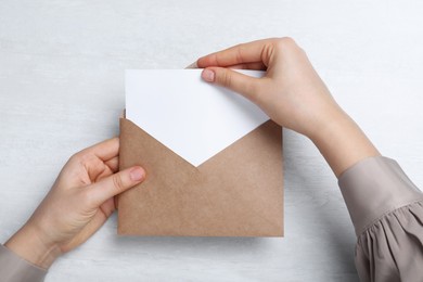 Woman taking card out of envelope at light table, top view