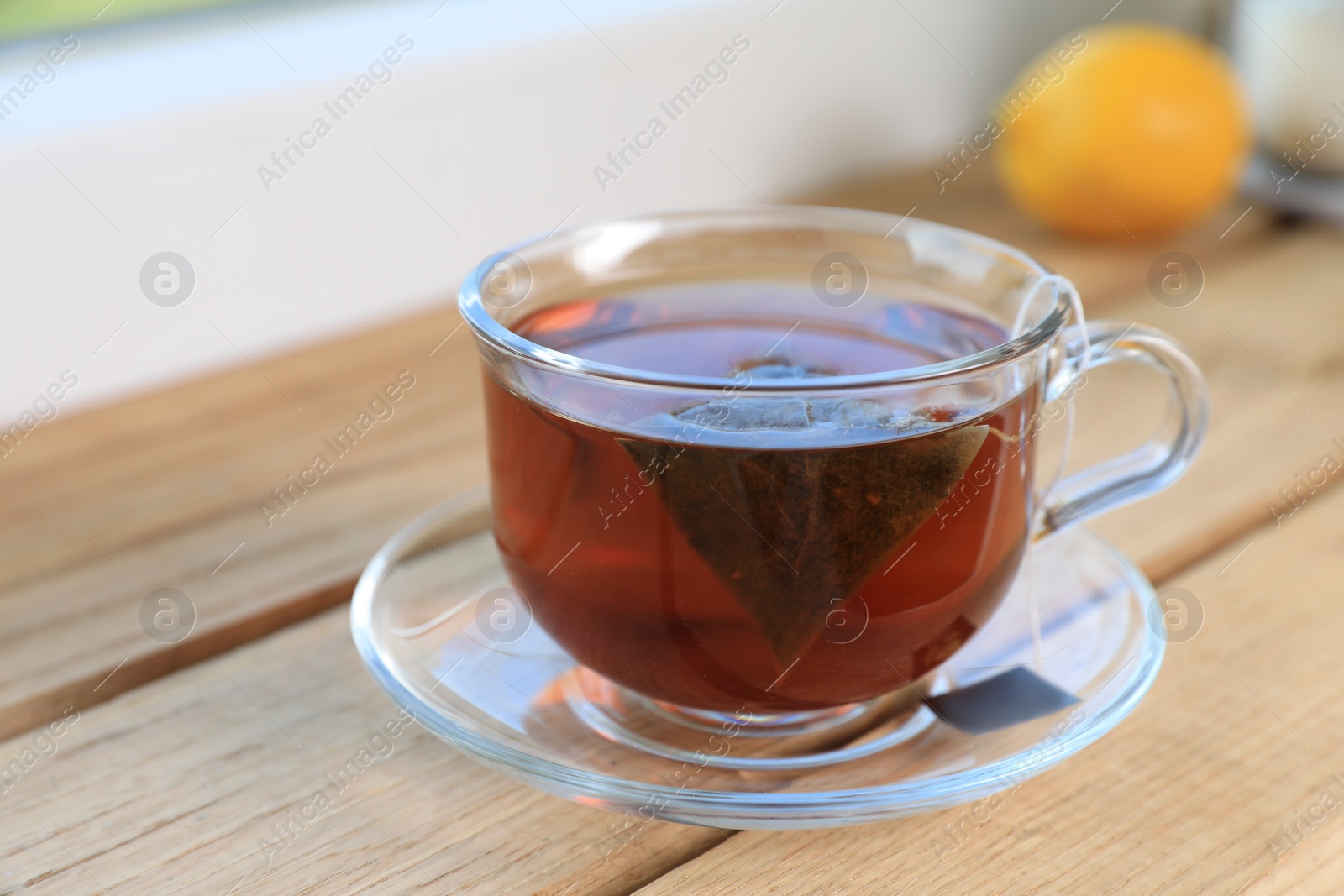 Photo of Bag of black tea in cup with hot water on wooden table indoors