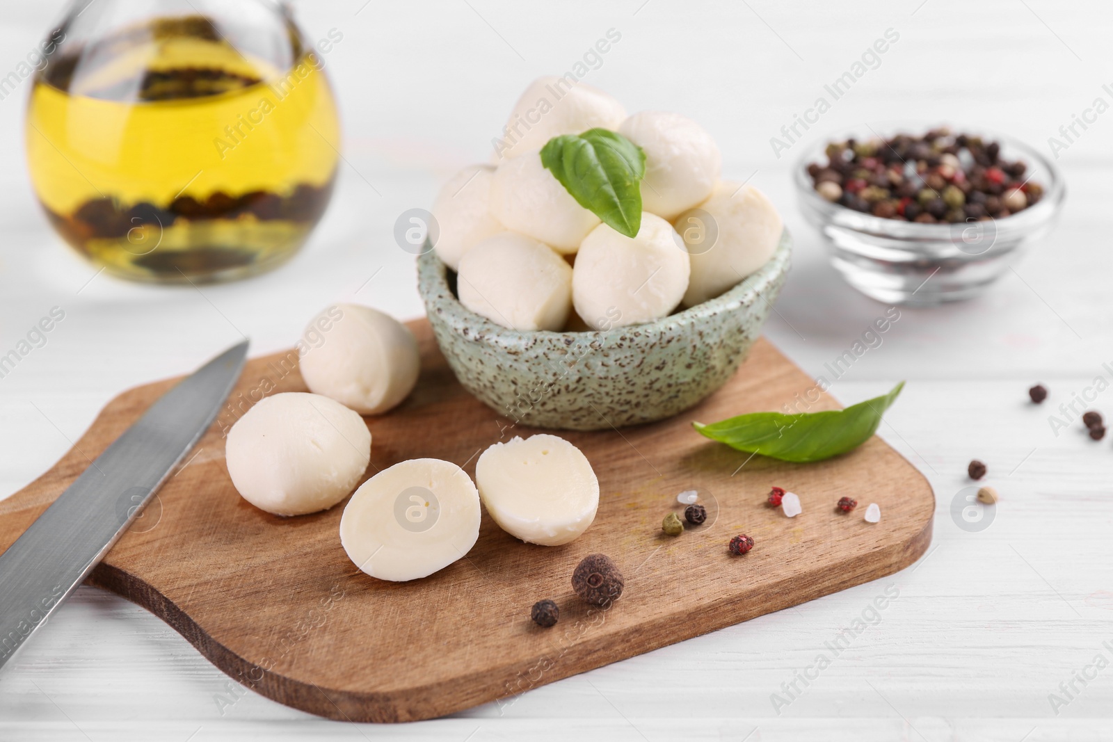 Photo of Tasty mozzarella balls, basil leaves and spices on white wooden table