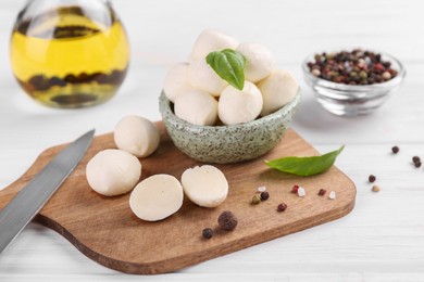 Photo of Tasty mozzarella balls, basil leaves and spices on white wooden table