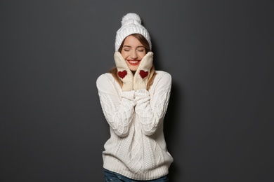 Photo of Beautiful young woman in warm sweater with hat and mittens on dark background