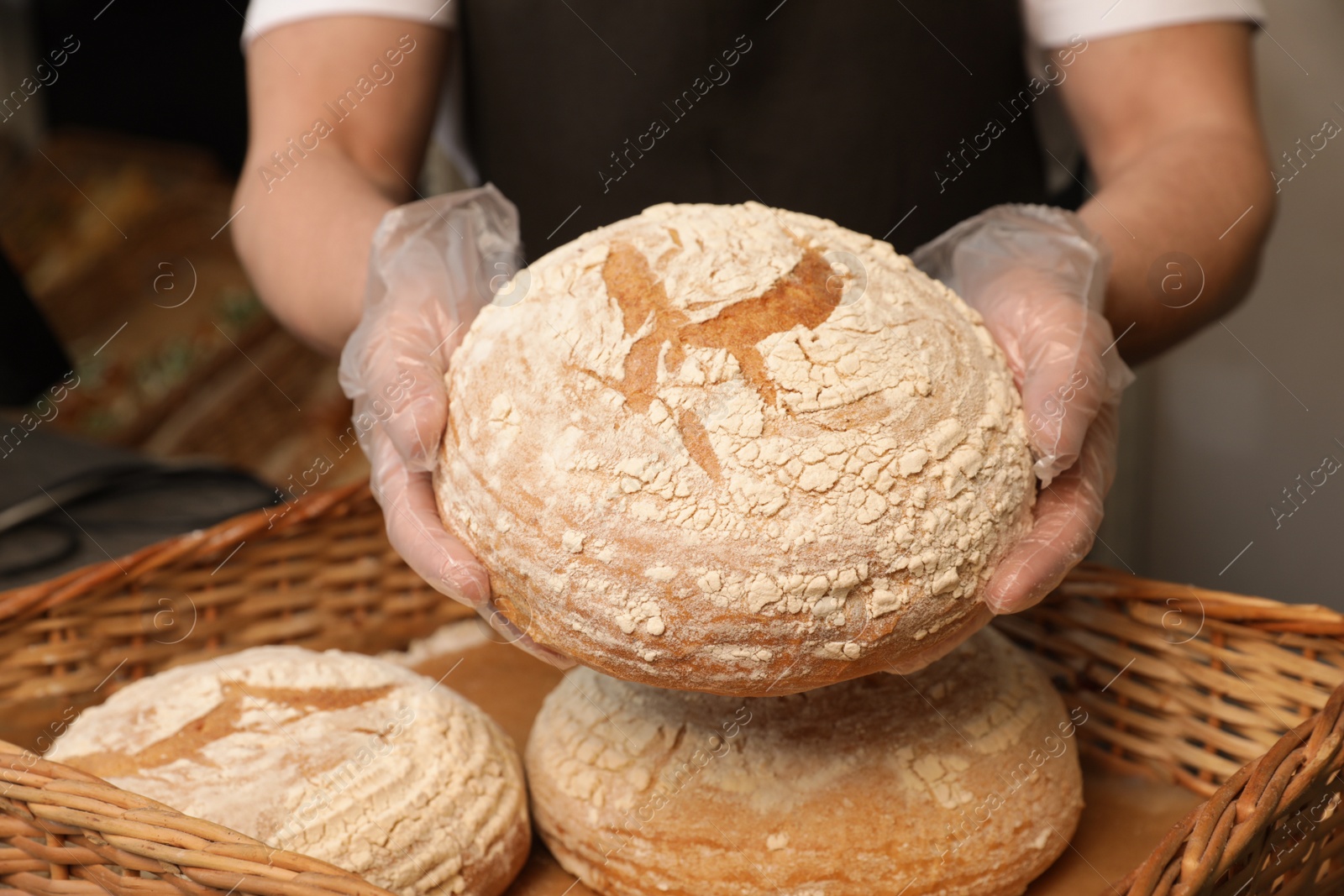 Photo of Professional baker holding loaf of bread over tray in store, closeup