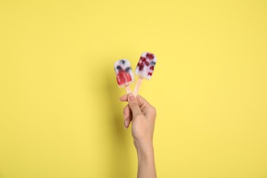 Photo of Woman holding berry popsicle on yellow background, closeup