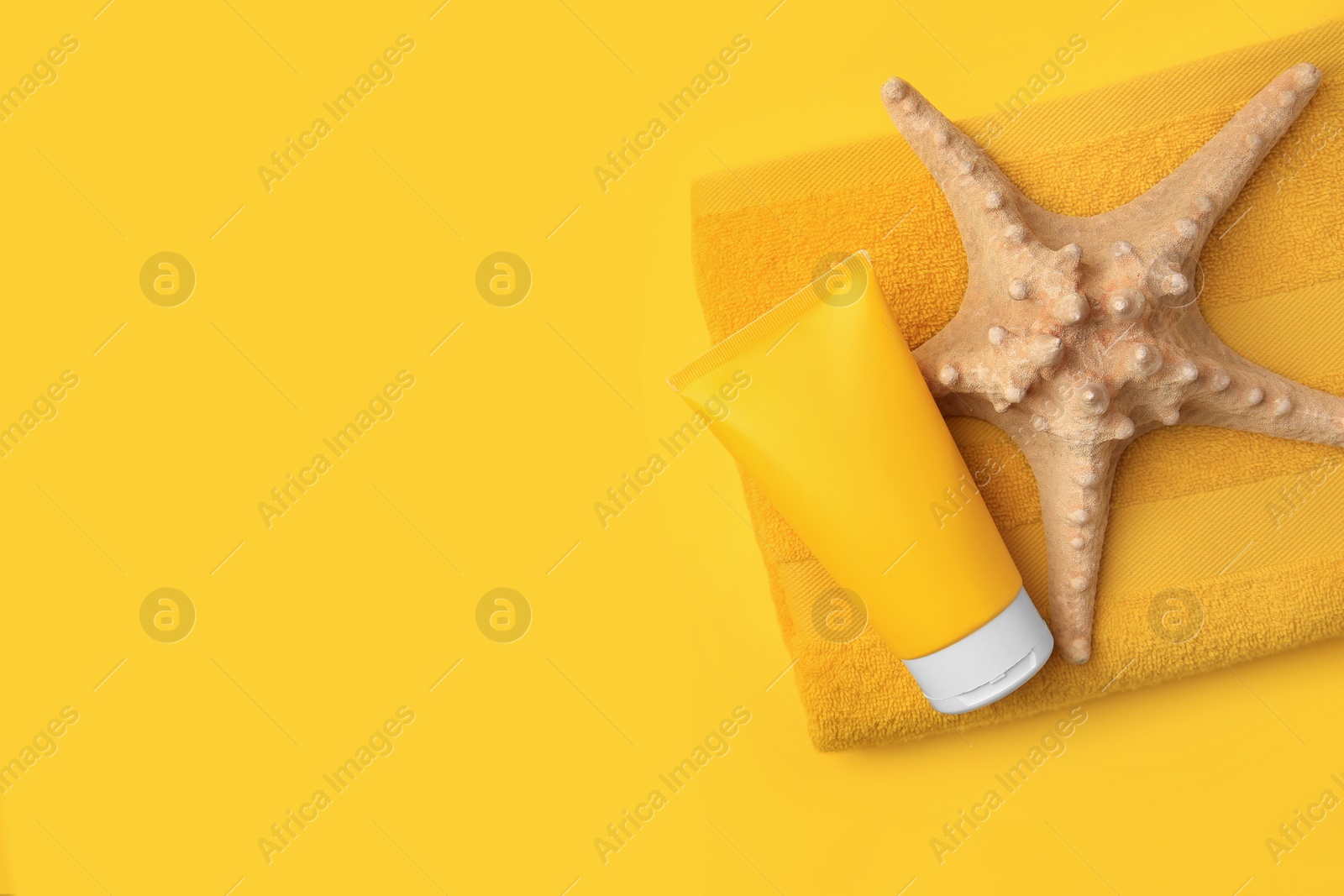 Photo of Tube of sunscreen, starfish and towel on orange background, top view with space for text. Sun protection