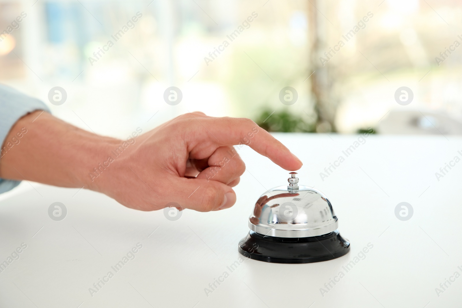 Photo of Young man ringing service bell on reception desk in hotel, closeup