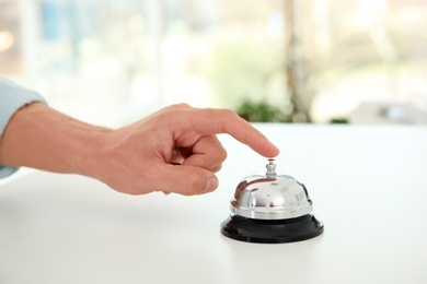 Photo of Young man ringing service bell on reception desk in hotel, closeup