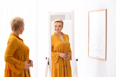 Photo of Beautiful mature woman looking at herself in large mirror indoors