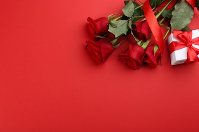 Photo of Beautiful roses and gift box on red background, flat lay with space for text. Valentine's Day celebration